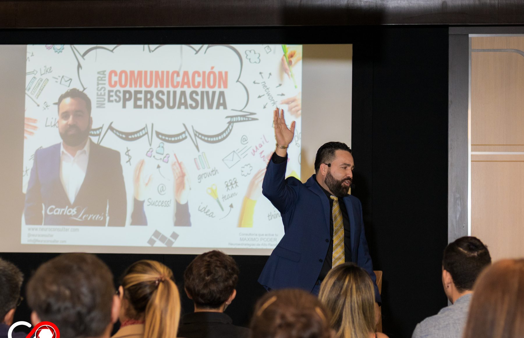 Carlos Leras speaking on stage in front of an audience, slide about persuasive communication behind him