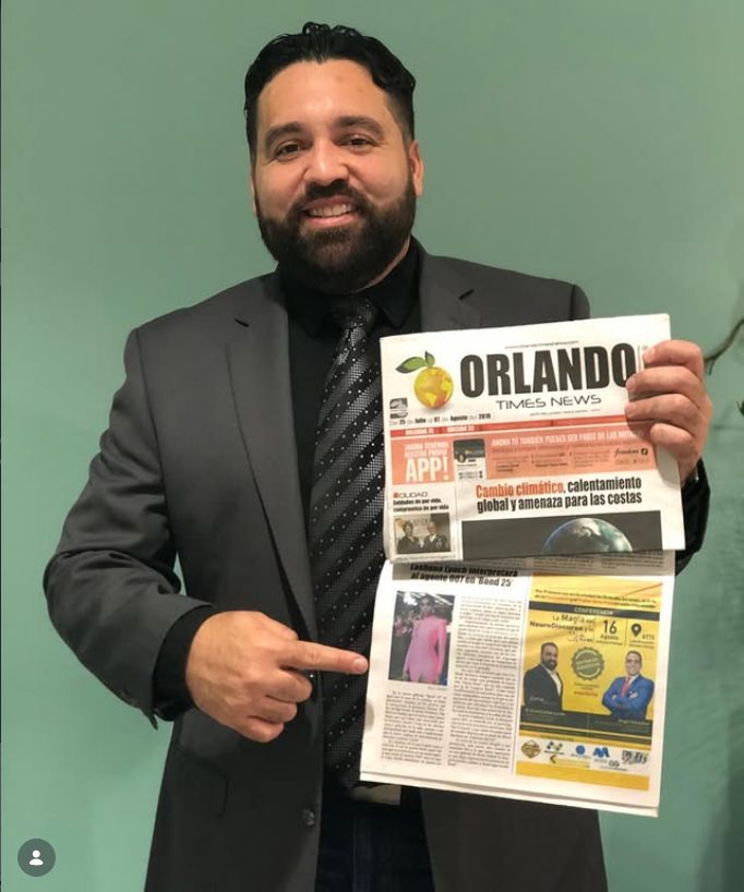 Carlos Leras holding a copy of Orlando Times News and pointing to his column